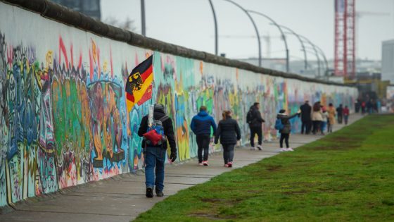 09 November 2019, Berlin: A man with a German flag in his backpack walks along the East Side Gallery, the former Berlin Wall. Photo: Gregor Fischer/dpa (Photo by Gregor Fischer/picture alliance via Getty Images)